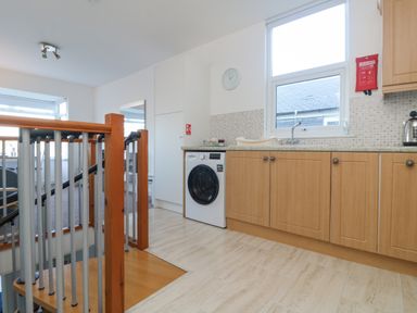 A kitchen with wooden cabinets a washing machine a sink and a window near a staircase at The Beach Hut in St Ives