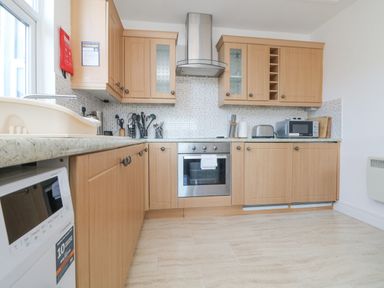 A kitchen with wooden cabinets a stainless steel oven microwave and utensils at The Beach Hut in St Ives