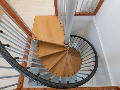A spiral wooden staircase with metal railings in a white room at The Beach Hut in St Ives