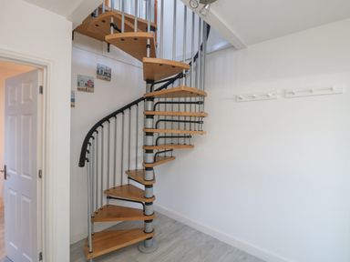 A spiral staircase with wooden steps and metal railings in a room with white walls and a coat rack on the wall at The Beach Hut in St Ives