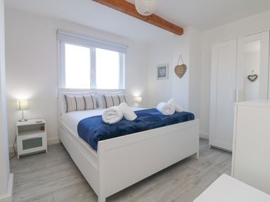 A bedroom with a white bed blue blanket rolled towels bedside tables lamps and a wardrobe at The Beach Hut in St Ives