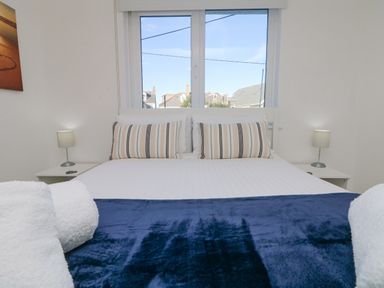 A bedroom with a bed and striped pillows under a window with a view of rooftops at The Beach Hut in St Ives