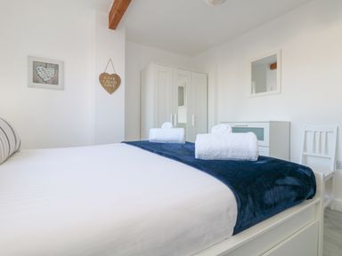 A bedroom with a bed with towels and a blue throw a white wardrobe white dresser and a chair at The Beach Hut in St Ives