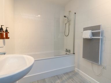 A bathroom with a bathtub shower combination a sink mounted soap dispensers and a wall-mounted heater at The Beach Hut in St Ives