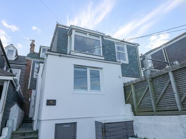 Exterior view of a multi-story house with white walls and slate roofing with wooden fencing on the side at The Beach Hut in St Ives