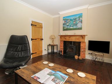 A living room with a black chair wooden door wood-burning stove television and a wooden coffee table with a magazine at Weybury Cottage Brewers Quay Harbour