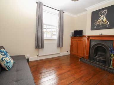 A room with wooden floor a sofa a window with curtains a fireplace and a small television at Weybury Cottage Brewers Quay Harbour