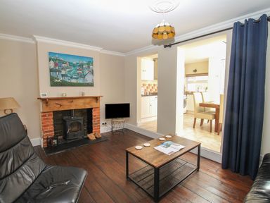 A living room with a fireplace a black leather chair a wooden coffee table and a view into a kitchen at Weybury Cottage Brewers Quay Harbour
