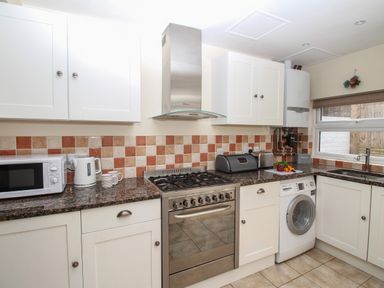 A kitchen with white cabinets a stove washing machine microwave and a window at Weybury Cottage Brewers Quay Harbour