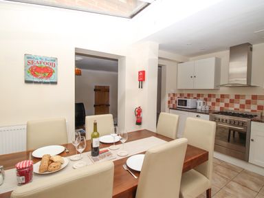 A kitchen and dining area with a wooden table set with plates glasses and bread a microwave stove and kettle are visible at Weybury Cottage in Brewers Quay Harbour