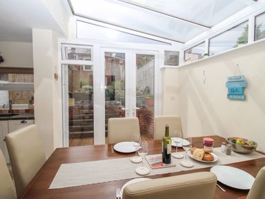 A dining area with a wooden table set with plates glasses wine bottle and food next to glass doors leading outside at Weybury Cottage Brewers Quay Harbour