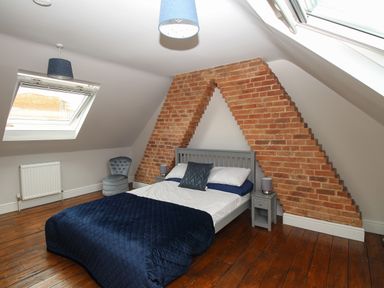 A bedroom with a bed against a brick wall under a sloped ceiling with skylight windows at Weybury Cottage in Brewers Quay Harbour