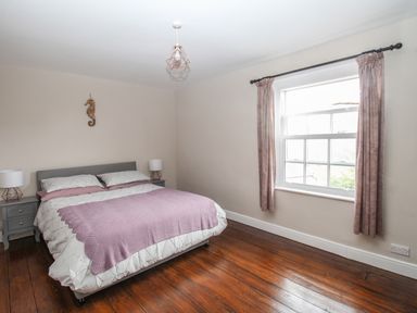 A bedroom with a double bed bedside tables lamps a window with curtains and wooden floor at Weybury Cottage Brewers Quay Harbour