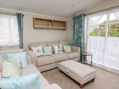 A living room with sofas cushions ottoman small round table and windows with blue curtains at Ystwyth 26 in Borth
