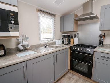 A kitchen with grey cabinets a microwave a toaster a kettle a coffee machine and a stove at Ystwyth 26 in Borth