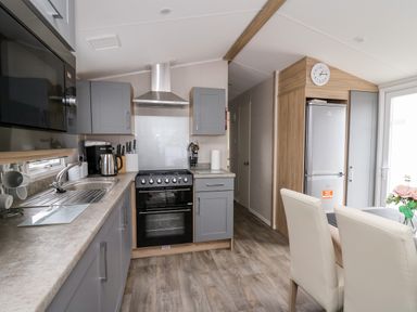 A kitchen with grey cabinets a black oven a stainless steel sink a refrigerator and a dining table with chairs at Ystwyth 26 in Borth
