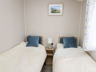 A bedroom with two single beds with blue cushions a small wooden nightstand with a lamp and a framed picture on the wall at Ystwyth 26 in Borth