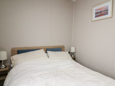 A bedroom with a double bed two bedside tables with lamps and a framed picture on the wall at Ystwyth 26 in Borth