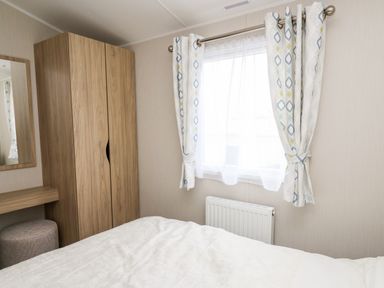A bedroom with a wooden wardrobe a window with patterned curtains and a bed at Ystwyth 26 in Borth