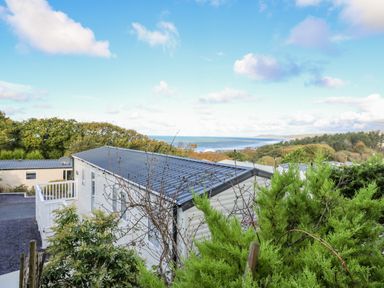 A mobile home with a grey roof surrounded by greenery and overlooking the sea at Ystwyth 26 in Borth