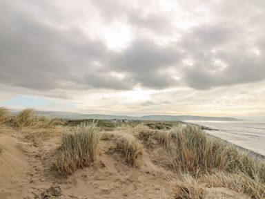 A sandy beach with grass tufts and a cloudy sky over the sea at Ystwyth 26 in Borth