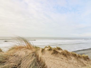A sandy beach with grass-covered dunes and waves in the sea at Ystwyth 26 in Borth