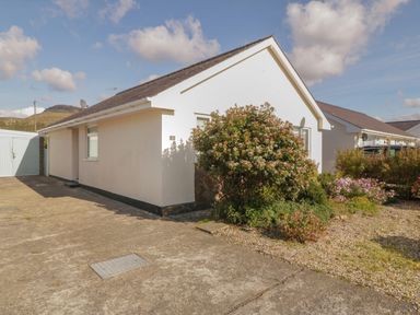 A single-story house with a concrete driveway and garden bushes at Seaside retreat in Porthmadog