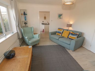 A living room with a blue sofa with cushions an armchair a wooden coffee table and a patterned rug at Seaside retreat in Porthmadog