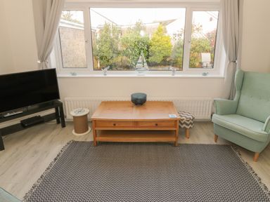A living room with a television on a stand a wooden coffee table a green armchair and a large window showing garden outside at Seaside retreat in Porthmadog