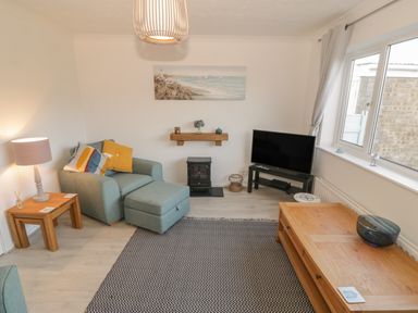 A living room with an armchair and ottoman a television on a stand and a wooden coffee table at Seaside retreat in Porthmadog