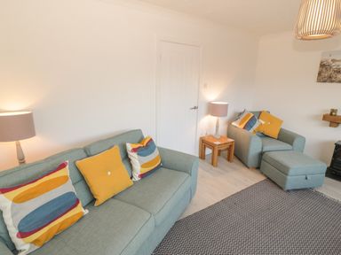 A living room with two blue sofas with yellow and patterned cushions two side tables with lamps and a patterned rug at Seaside retreat in Porthmadog