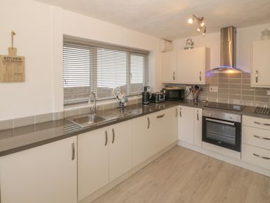 A kitchen with white cabinets a countertop sink stove oven microwave toaster and a window with blinds at Seaside retreat in Porthmadog