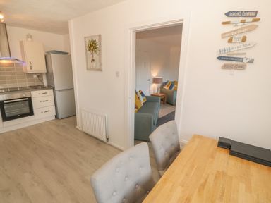 A kitchen with a dining table and chairs next to a living room with sofas and a lamp at Seaside retreat in Porthmadog