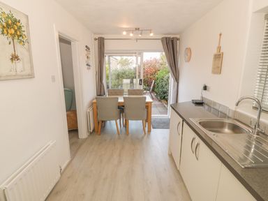 A kitchen with a sink and countertop and a dining table with four chairs near a sliding glass door at Seaside retreat in Porthmadog