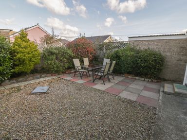 A backyard with a gravel area a tiled patio with a table and six chairs and surrounding bushes at Seaside retreat in Porthmadog