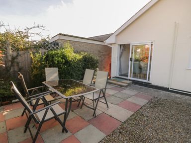 A patio area with a glass table and six chairs next to a house with sliding doors at Seaside retreat in Porthmadog