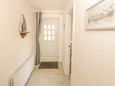 A hallway with a white door at the end a striped curtain a sailboat decoration on the wall a radiator and a framed picture on the wall at Seaside retreat in Porthmadog