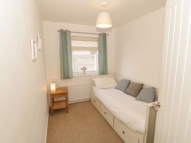 A small bedroom with a single bed cushions bedside table lamp window and curtains at Seaside retreat in Porthmadog