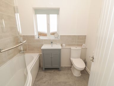 A bathroom with a bathtub a sink with a grey cabinet and a toilet at Seaside retreat in Porthmadog