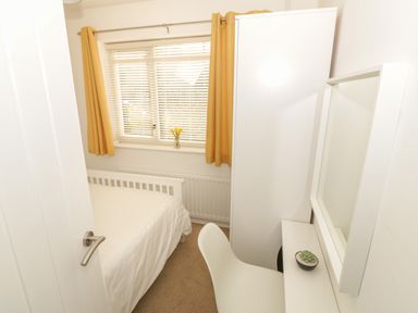 A small bedroom with a bed a white wardrobe a desk with a mirror and a chair with yellow curtains at Seaside retreat in Porthmadog