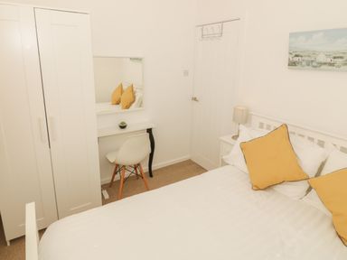 A bedroom with a white bed with yellow pillows a white wardrobe a small desk with a chair and a mirror Seaside retreat in Porthmadog