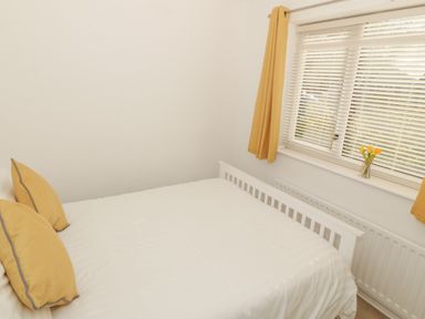 A bedroom with a white bed and yellow pillows next to a window with yellow curtains and a vase of flowers at Seaside retreat in Porthmadog