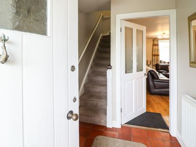 An entryway with a partially open white door showing stairs and an open doorway to a living room with leather sofas at Artro View in Llanbedr
