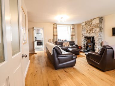 A living room with brown leather sofas a stone fireplace and wooden floor at Artro View in Llanbedr