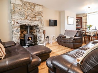 A living room with leather sofas a stone fireplace and a wall-mounted television at Artro View in Llanbedr