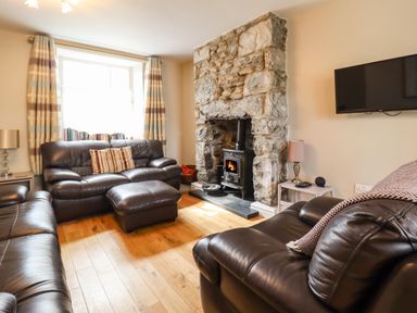 A living room with leather sofas a stone fireplace with a stove a mounted tv and a window with striped curtains at Artro View in Llanbedr