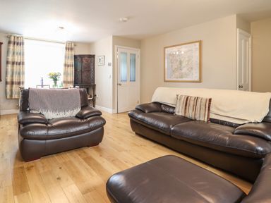 A living room with leather sofas a wooden floor a dining table with flowers and striped curtains at Artro View in Llanbedr