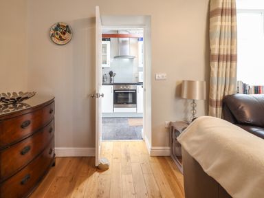 A view from a living room into a kitchen with a wooden chest of drawers a lamp a doorstop and a leather sofa at Artro View in Llanbedr