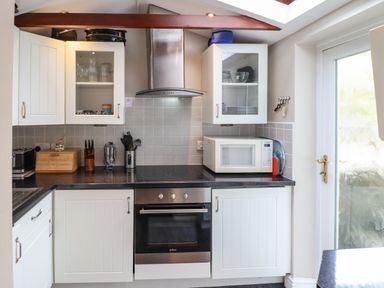A kitchen with white cabinets a black countertop a microwave oven an electric stove a toaster and a bread box at Artro View in Llanbedr