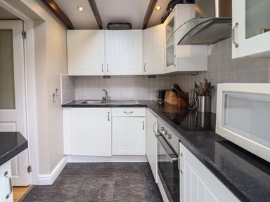 A kitchen with white cabinets black countertops a sink microwave oven and kitchen utensils at Artro View in Llanbedr